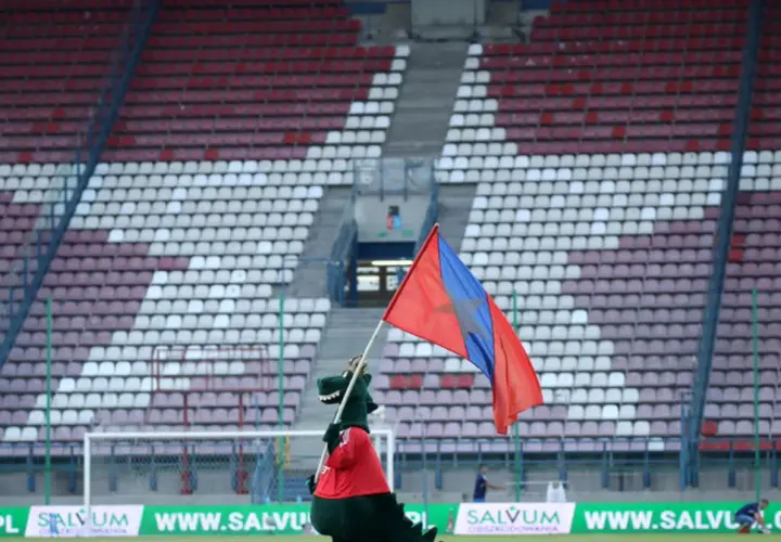 Maskotka Wisły Kraków z flagą na tle stadionu.