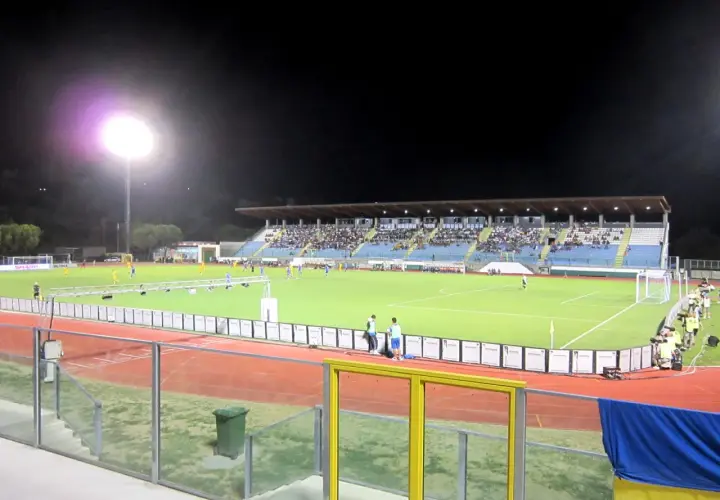 Wieczorny mecz na stadionie w San Marino. Piłkarze biegają po zielonej murawie, a trybuny wypełnia publiczność.
