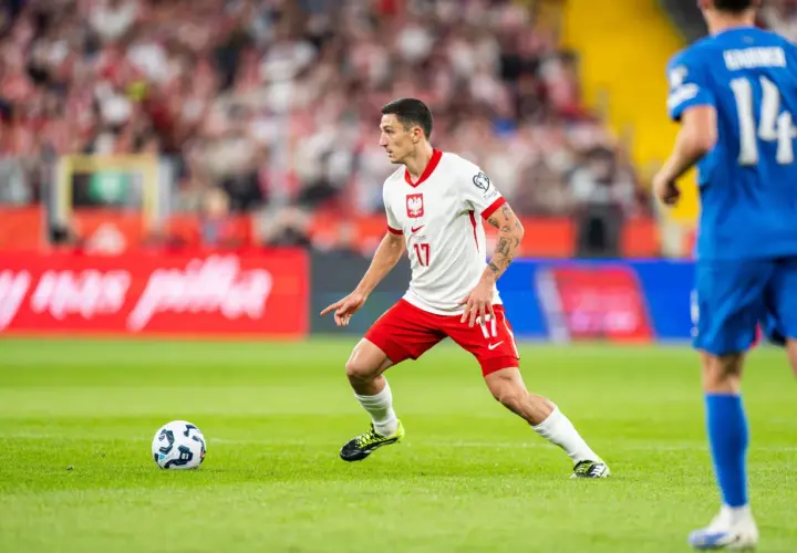 Bartosz Slisz w białej koszulce z orłem na piersi, w akcji na boisku.