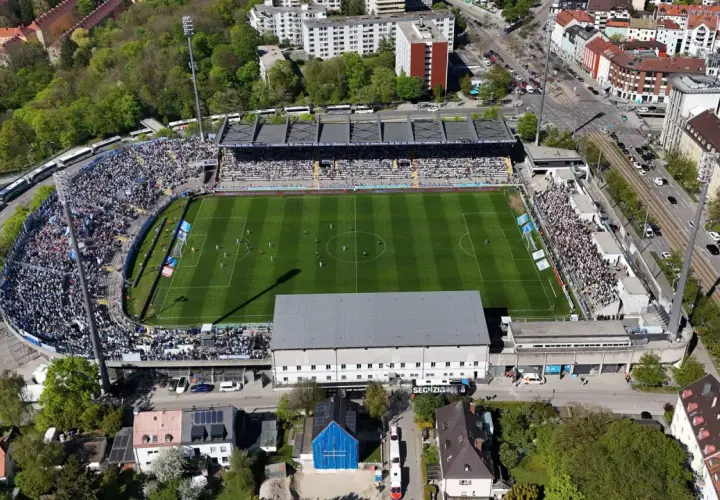 Widok z lotu ptaka na tętniący życiem tsv monachium stadion, pełen kibiców. Piłkarze rozgrywają mecz na zielonej murawie.