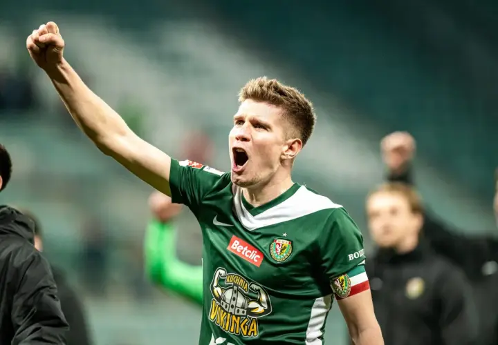 Piłkarz w zielonej koszulce z podniesioną pięścią świętuje awans do ekstraklasy.