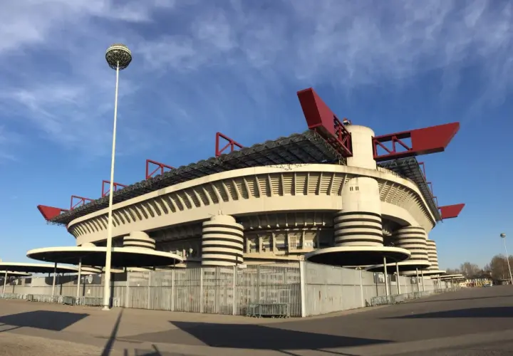Stadion AC Milan, San Siro, z charakterystycznymi czerwonymi elementami dachu i kulistą latarnią, prezentuje się imponująco na tle błękitnego nieba.