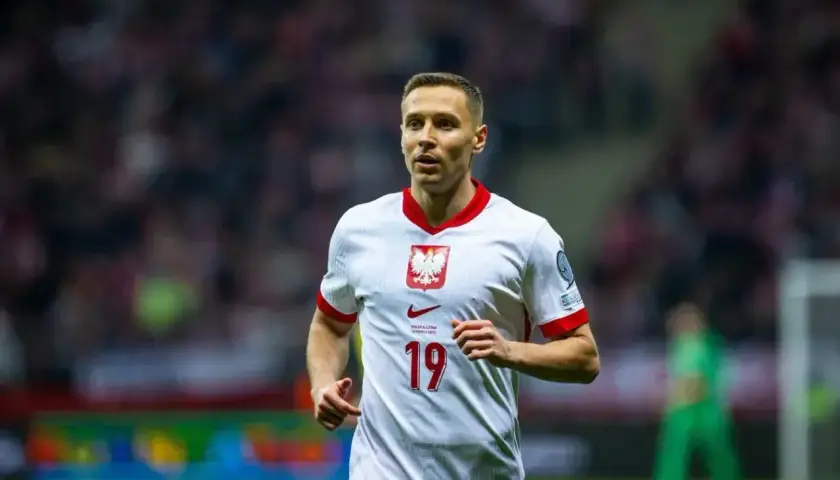 Piłkarz Przemysław Frankowski w białej koszulce z numerem 19, reprezentujący Polskę. Jego obecne drużyny to RC Lens i reprezentacja Polski.