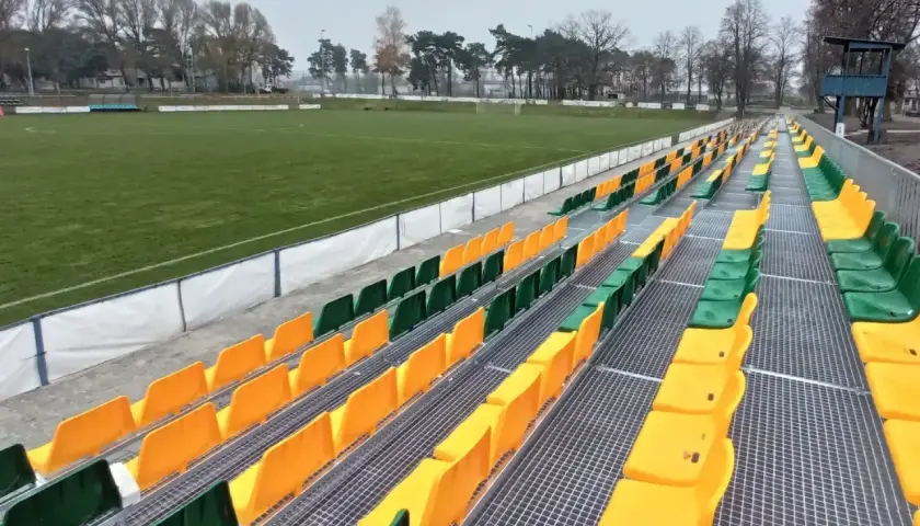 Puste trybuny stadionu Lechii Zielona Góra, z rzędami zielonych i żółtych krzesełek.