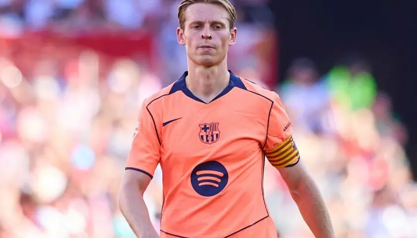 Frenkie de Jong w pomarańczowej koszulce FC Barcelony z opaską kapitana na ramieniu, skupiony na boisku.