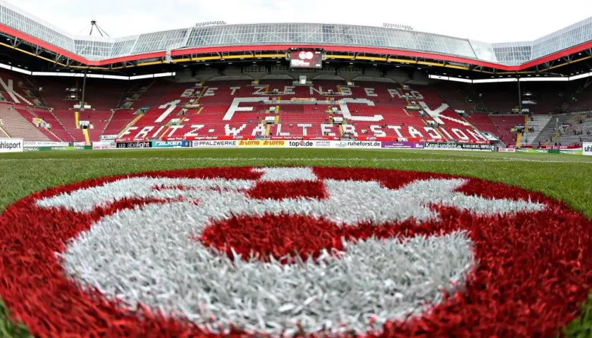 Na murawie stadionu Fritz-Walter-Stadion, symbol klubu FC Kaiserslautern. Czerwono-białe barwy drużyny dominują na trybunach i boisku.