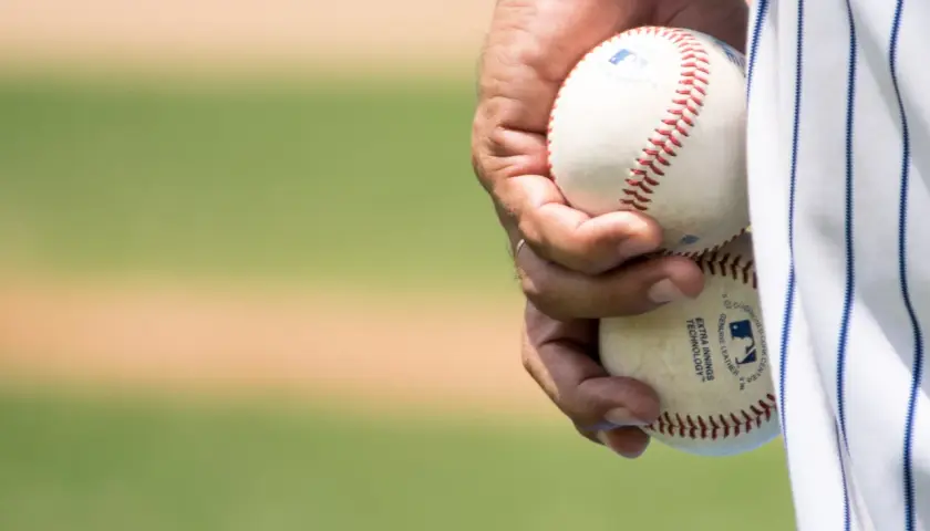 Dłoń trzyma dwie piłki baseballowe, gotowe do gry. Widać napis "EXTRA INNINGS TECHNOLOGY", świadczący o zaawansowanej technice niskiej piłki.