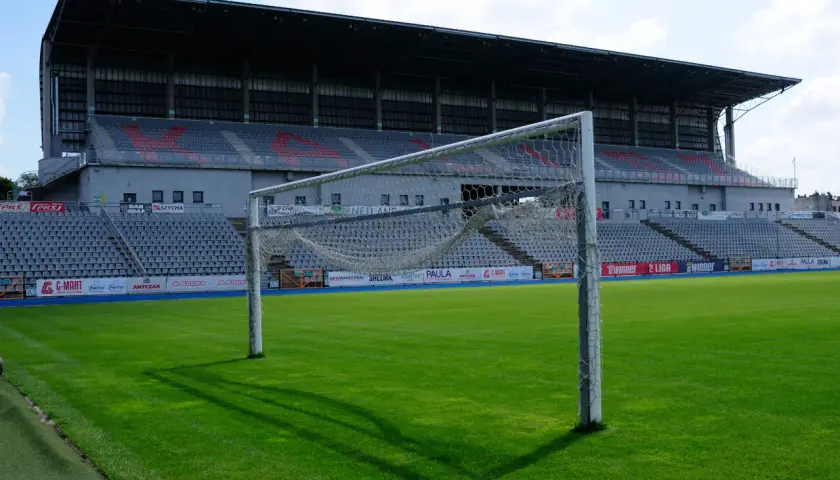 Pusta bramka na zielonej murawie stadionu KKS Kalisz. W tle trybuny i zadaszenie.