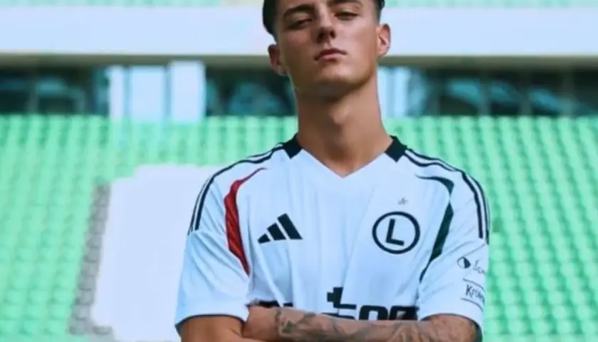 Kacper Urbański, młody piłkarz w białej koszulce z czarnymi pasami, z dumą prezentuje swoje tatuaże.