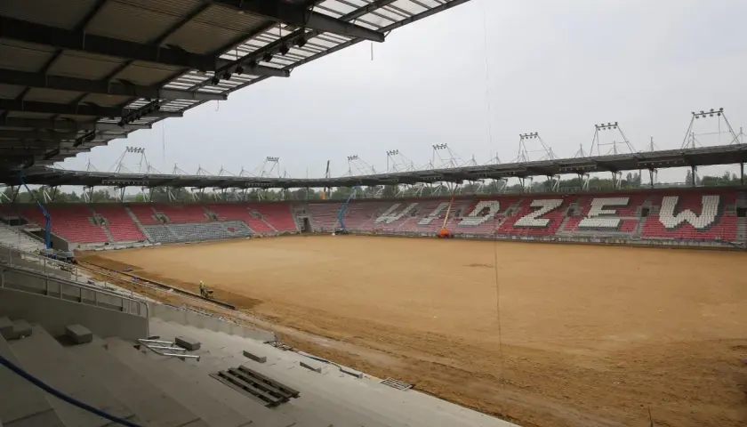 Trwa rozbudowa stadionu Widzewa. Na piaszczystym boisku widać prace budowlane i krzesełka w barwach klubu.