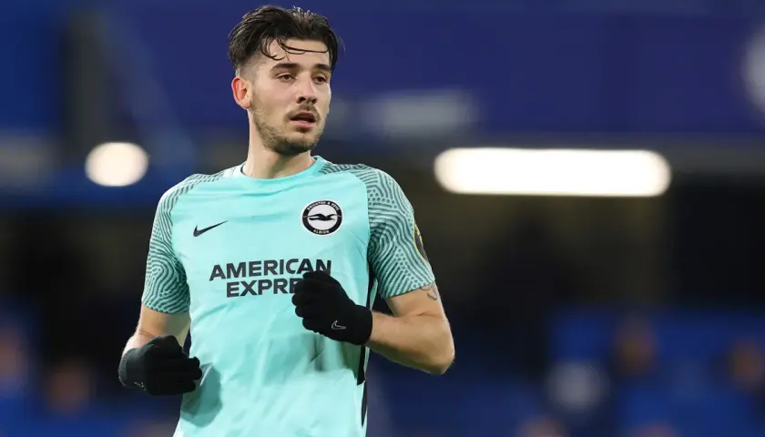 Piłkarz Jakub Moder w koszulce Brighton, zmagający się z kontuzją, na tle niebieskich trybun.