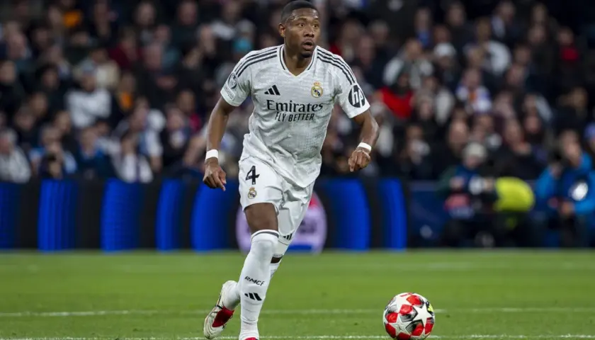 David Alaba w białej koszulce Realu Madryt z numerem 4 biegnie z piłką na murawie, skupiony na grze.