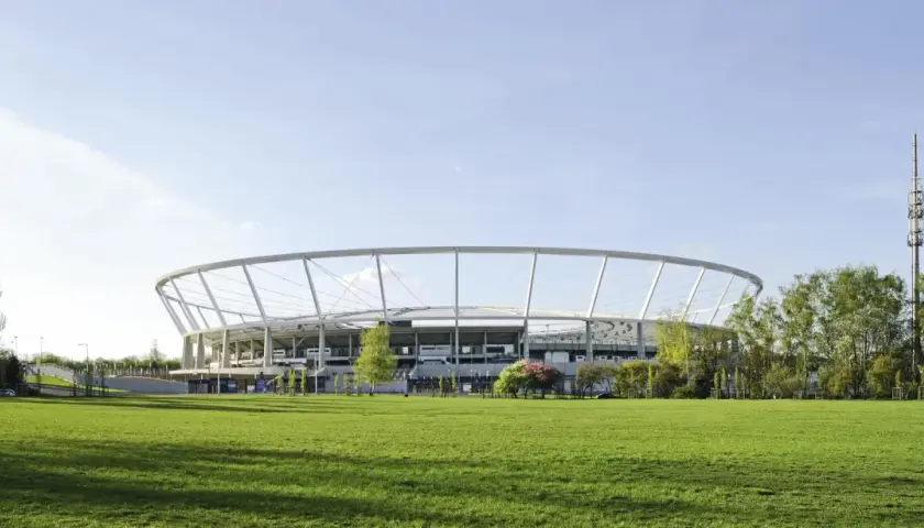 Nowoczesny Stadion Śląski otoczony zielenią, z charakterystyczną, okrągłą konstrukcją dachu.