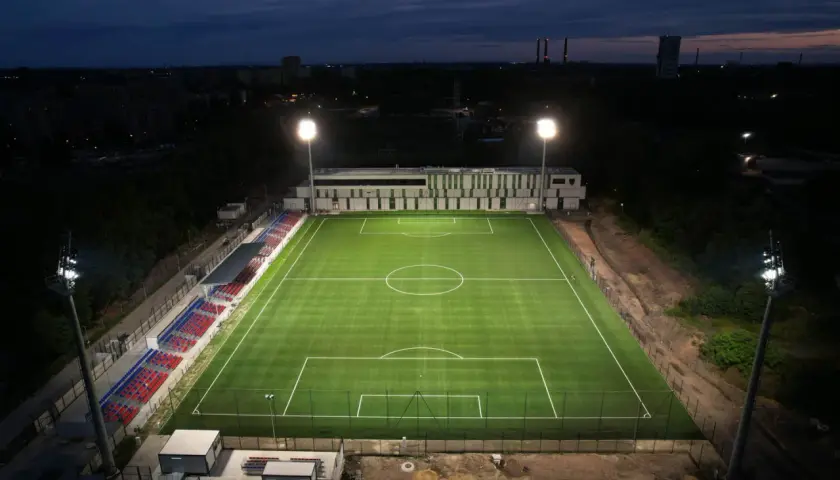 Piękny, oświetlony stadion Polonii Bytom nocą. Zielona murawa i czerwono-niebieskie trybuny czekają na kibiców.