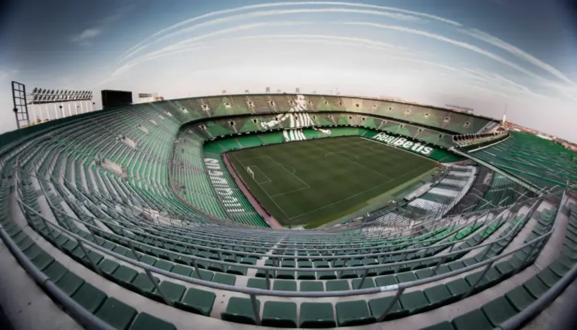 Puste trybuny stadionu Real Betis, zielone krzesełka tworzą mozaikę pod błękitnym niebem.