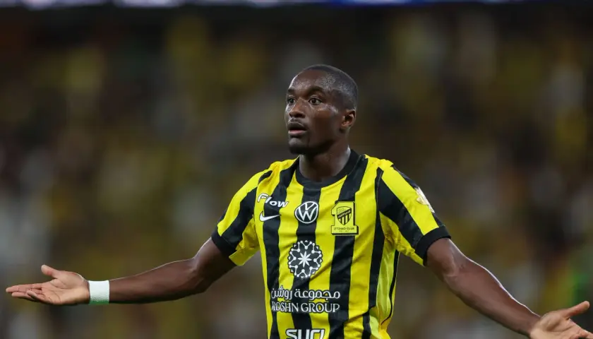 Piłkarz Moussa Diaby w żółto-czarnej koszulce z logo Iттihad Club, z otwartymi dłońmi, gotowy do gry.