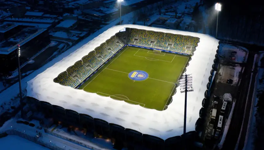 Zimowy wieczór na stadionie Gdynia Arka. Oświetlony stadion z zieloną murawą i śniegiem na trybunach, gotowy na mecz Bałtyk Gdynia.