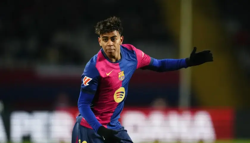 Młody zawodnik FC Barcelona w charakterystycznej koszulce, z numerem 19 na spodenkach, gestykuluje na boisku.