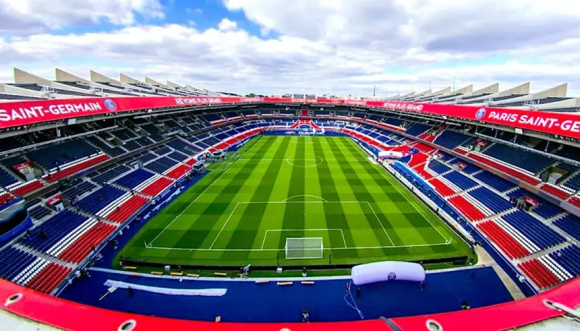 Pusta trybuna stadionu Parc des Princes, z czerwono-niebieskimi siedzeniami i zieloną murawą, gotowa na mecz Paris Saint-Germain.