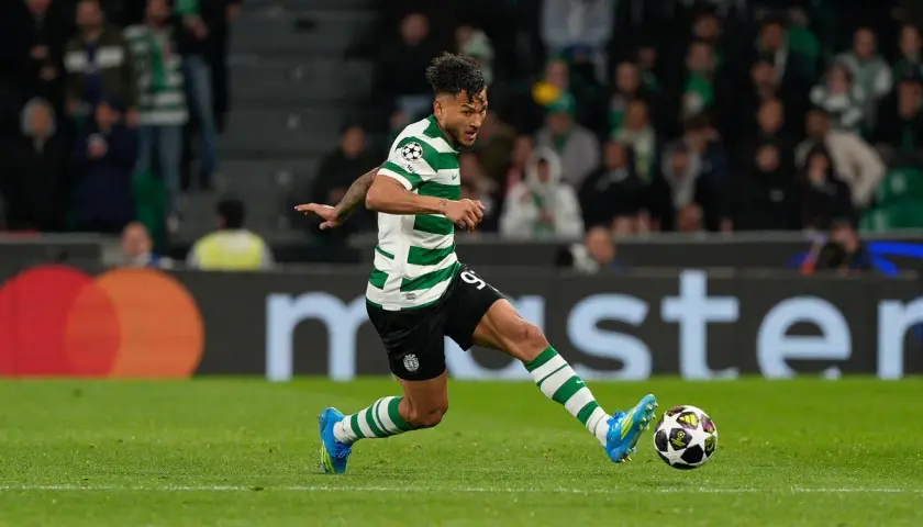 Piłkarz Sporting CP w zielono-białej koszulce drybluje z piłką na boisku.