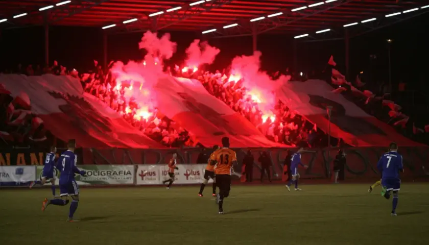 Chrobry Głogów stadion w ogniu rac! Kibice tworzą biało-czerwoną oprawę, a piłkarze grają na murawie.