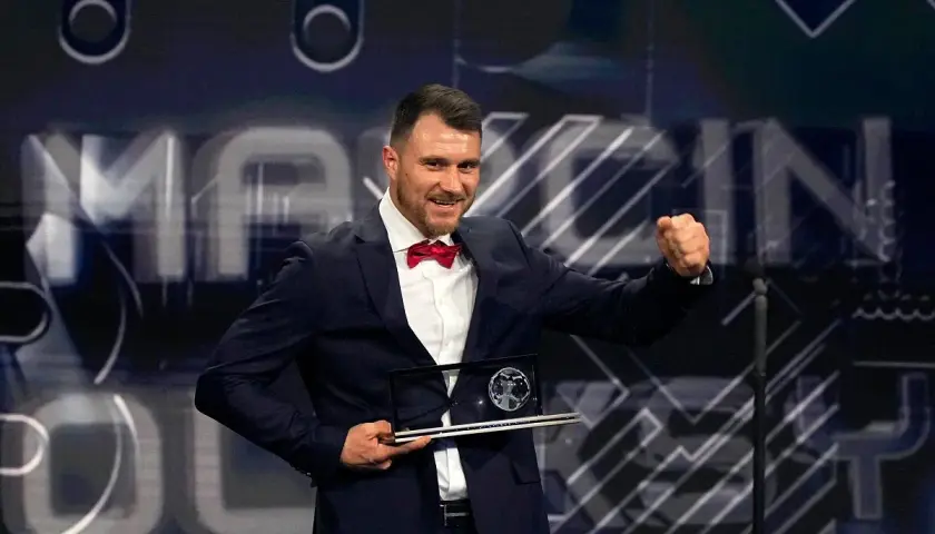 Piłkarz w garniturze z czerwoną muszką odbiera nagrodę Ferenca Puskasa, ciesząc się z sukcesu.