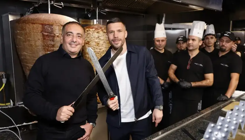 Lukas Podolski z nożami w ręku, obok niego pracownicy jego restauracji z kebabem.