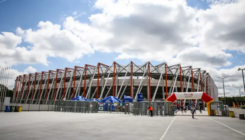 Nowoczesna chorten arena w Białymstoku, z charakterystyczną, ażurową konstrukcją dachu. Przed wejściem bramki obrotowe i łuk z logo stadionu.