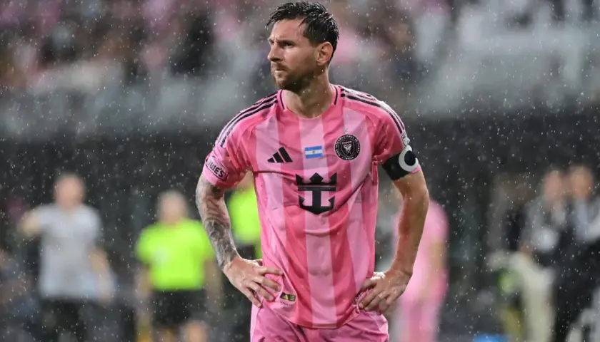 Lionel Messi w różowej koszulce Interu Miami, stojący w deszczu. Wygląda na zamyślonego, być może z powodu niedawnej kontuzji.