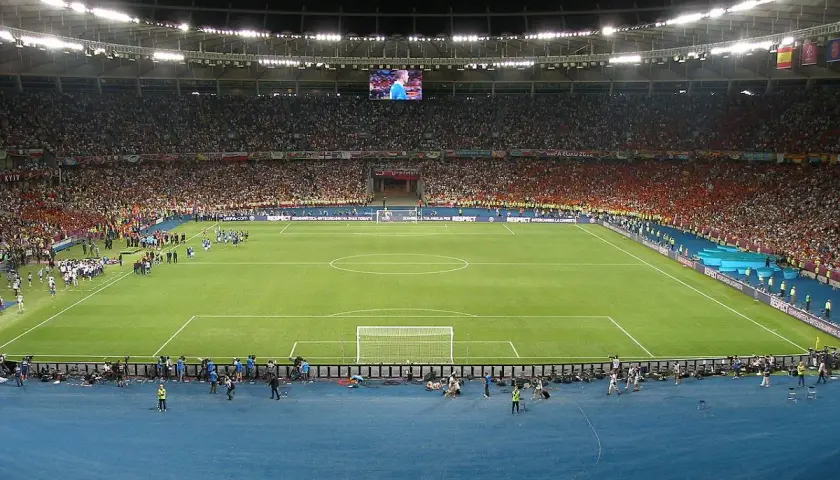 Piłkarze wychodzą na murawę stadionu olimpijskiego w Kijowie. Tłumy kibiców na trybunach, wielki ekran nad boiskiem.