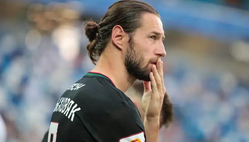 Grzegorz Krychowiak w czarnej koszulce, z włosami związanymi w kok, zamyślony na boisku.