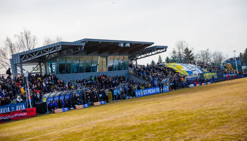 Widok na trybuny stadionu Avia Świdnik, wypełnione kibicami. W tle widać zadaszenie i drzewa.