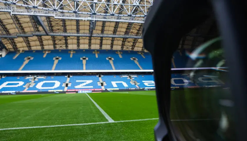 Pusta trybuna stadionu Lecha Poznań. Widoczne niebieskie sektory i miejsca, zielona murawa.