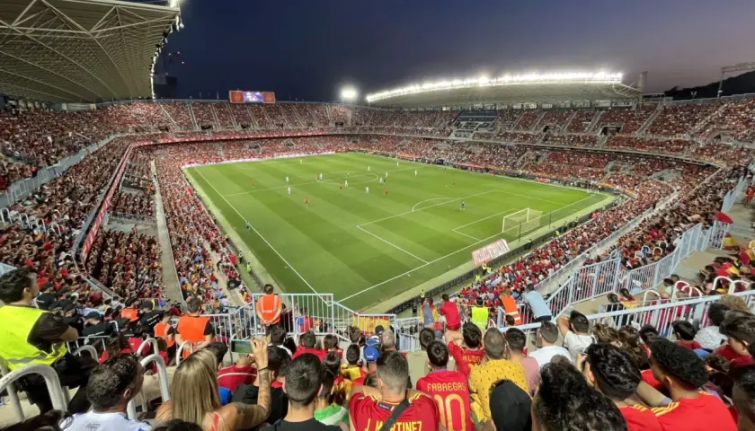 Widok z trybun na pełny stadion **Estadio La Rosaleda** podczas meczu piłki nożnej. Tłum kibiców w czerwonych barwach wypełnia trybuny.