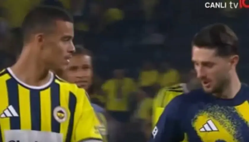 Piłkarze w żółto-granatowych strojach, jeden z nich to Mason Greenwood, rozmawiają na boisku.