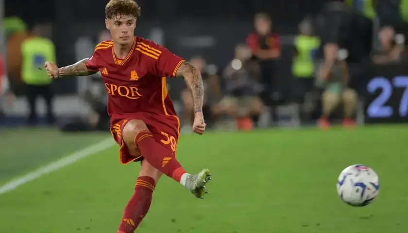 Nicola Zalewski w akcji, kopie piłkę na boisku w czerwonej koszulce AS Roma.