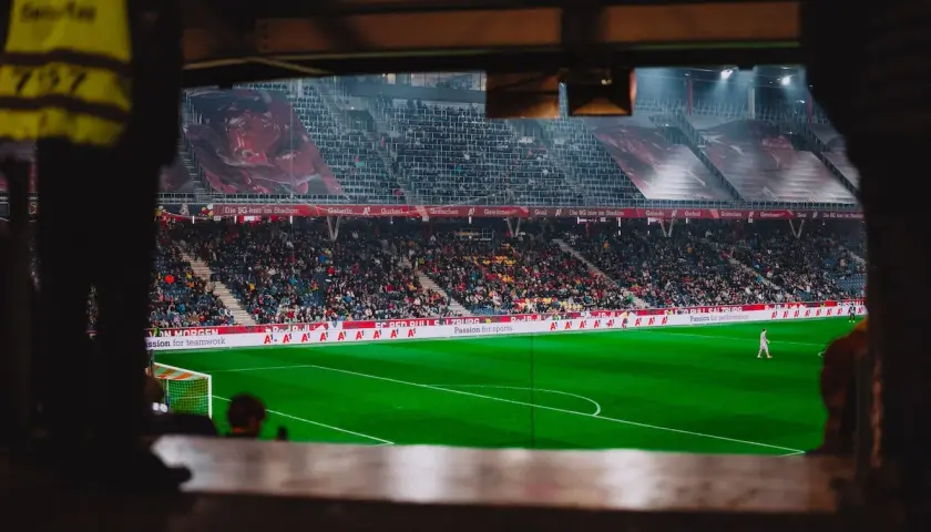 Piłkarz na boisku podczas meczu Wolfsberger – RB Salzburg. Trybuny pełne kibiców, wielkie banery na stadionie.