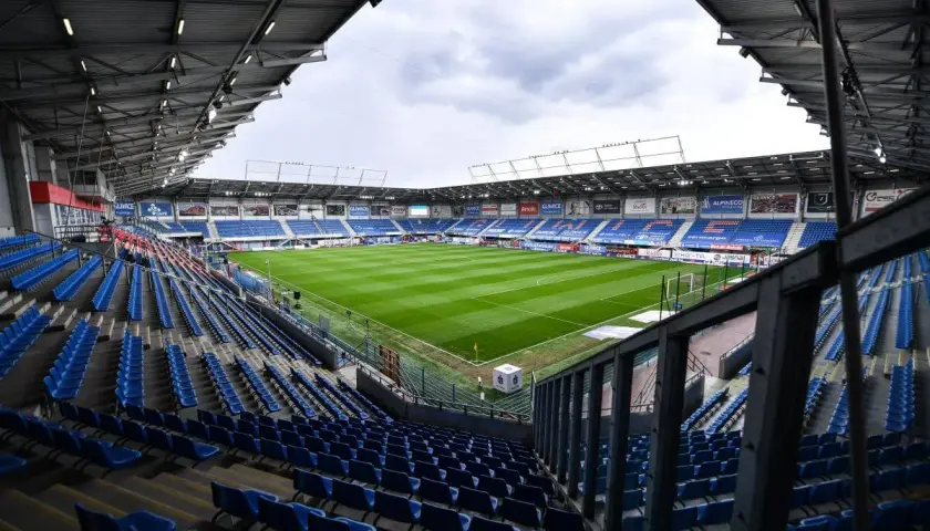 Puste trybuny stadionu Piasta Gliwice czekają na kibiców. Zielona murawa boiska lśni w blasku dnia.