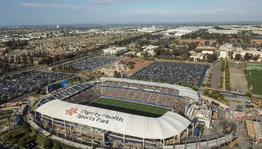 Widok z lotu ptaka na Dignity Health Sports Park, pełen widzów stadion piłkarski otoczony parkingami i miejską zabudową.