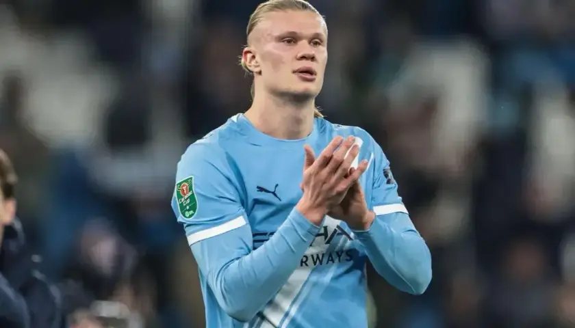 Erling Haaland w błękitnej koszulce Manchesteru City, z pucharem Carabao Cup na rękawie, klaszcze na boisku.