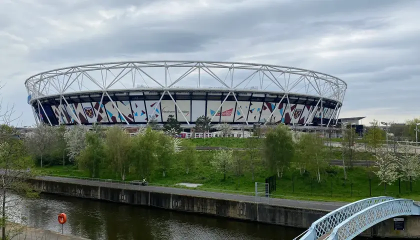 Ogromny stadion West Ham United z charakterystycznym logo klubu, otoczony zielenią i kanałem wodnym.
