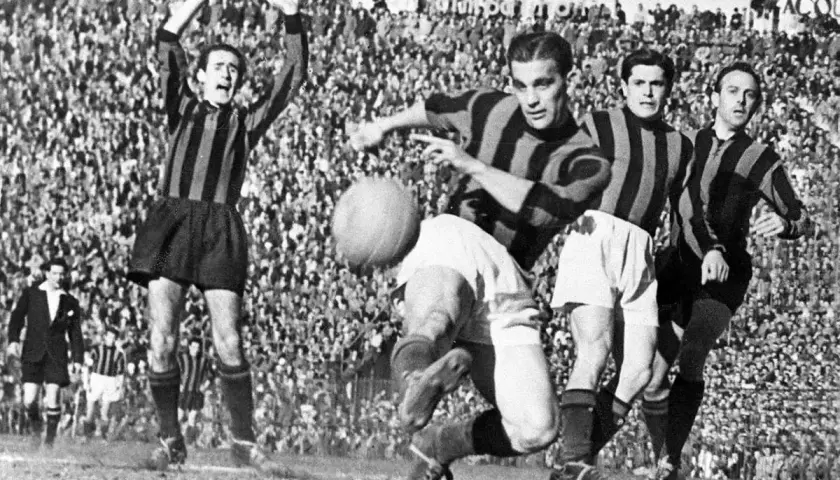 A.C. Milan – zawodnicy w akcji. Piłkarze w pasiatych koszulkach walczą o piłkę na tle trybun pełnych kibiców.