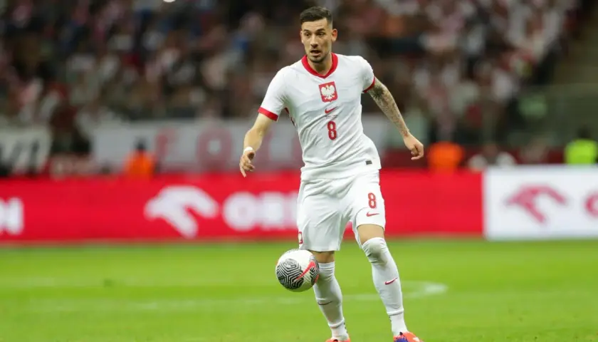 Jakub Moder w białej koszulce z numerem 8, z piłką przy nodze na boisku.