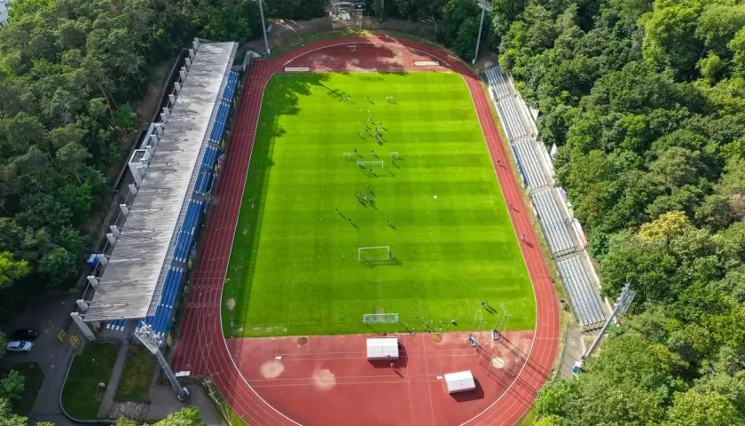 Piłkarze trenują na zielonej murawie stadionu Floty Świnoujście, otoczonego drzewami.