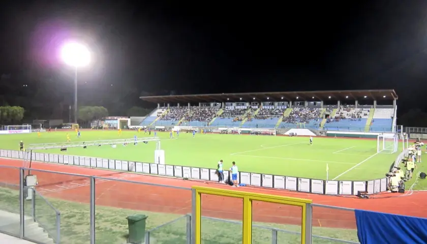 Wieczorny mecz na stadionie w San Marino. Piłkarze biegają po zielonej murawie, a trybuny wypełnia publiczność.
