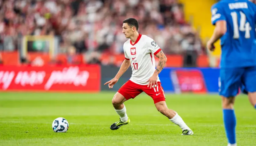 Bartosz Slisz w białej koszulce z orłem na piersi, w akcji na boisku.