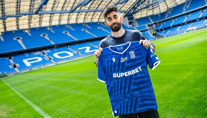 Ali Gholizadeh prezentuje nową koszulkę Lecha Poznań na tle stadionu.