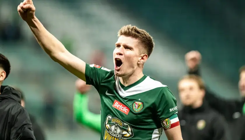 Piłkarz w zielonej koszulce z podniesioną pięścią świętuje awans do ekstraklasy.