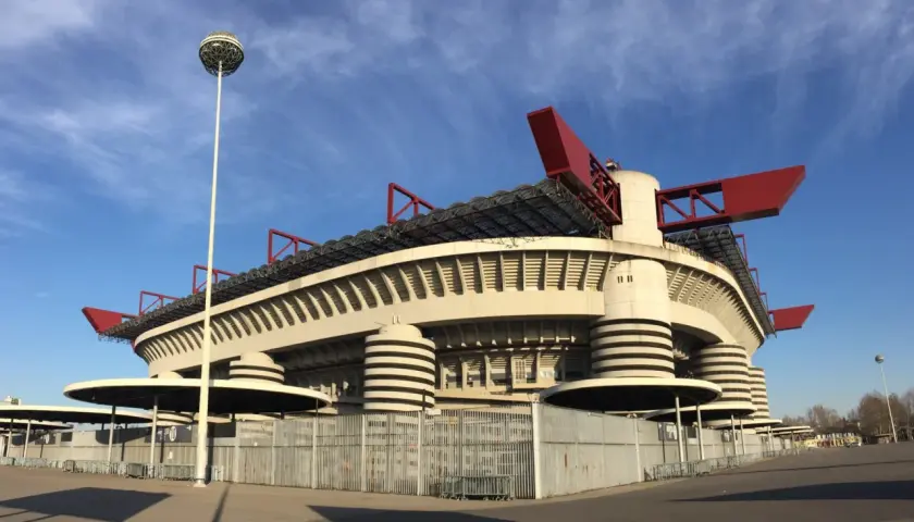 Stadion AC Milan, San Siro, z charakterystycznymi czerwonymi elementami dachu i kulistą latarnią, prezentuje się imponująco na tle błękitnego nieba.