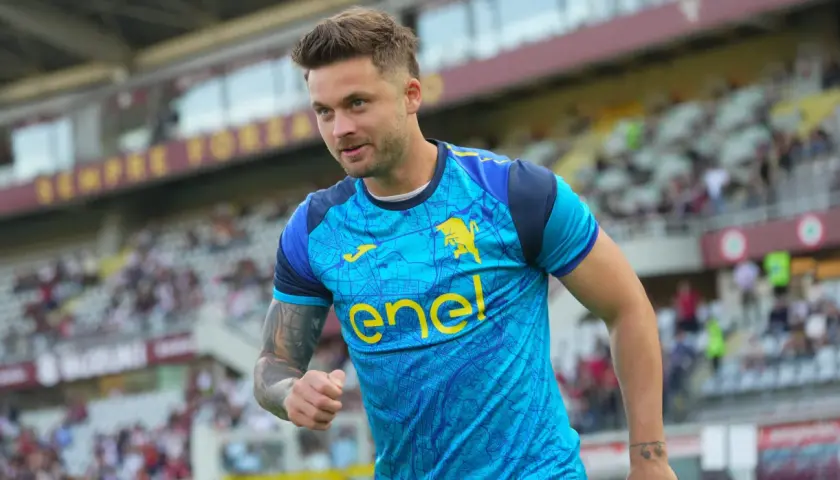 Piłkarz w błękitnej koszulce z żółtym logo "enel" i bykiem, widać trybuny stadionu. To moment, kiedy gra Linetty.